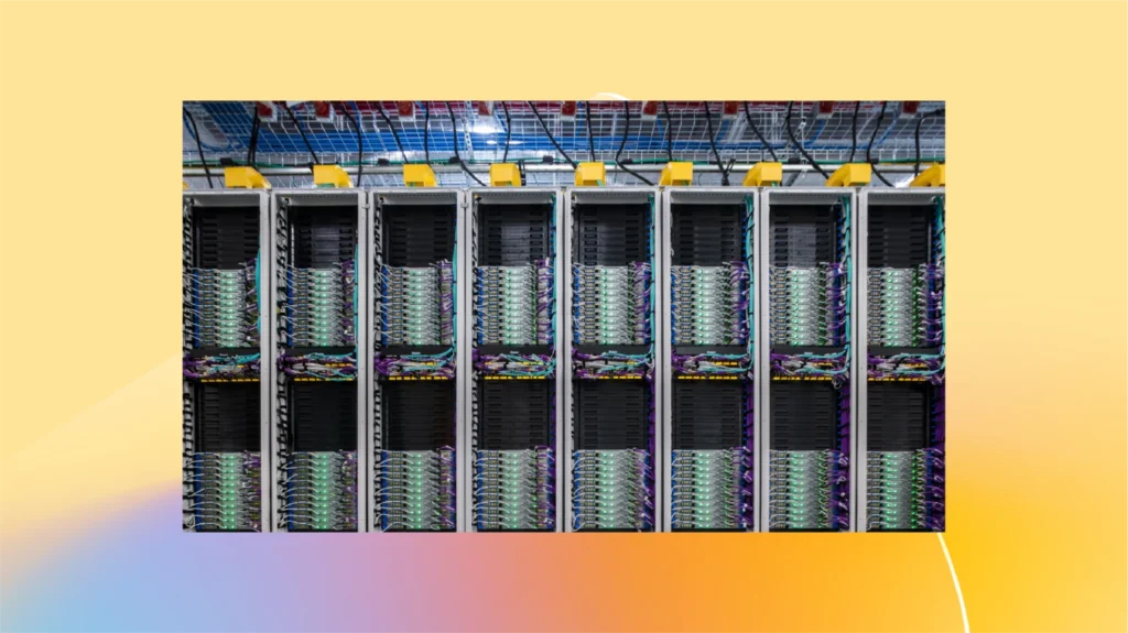 A row of large server racks with numerous cables and hardware components in a brightly lit data center, set against a yellow and orange gradient background.