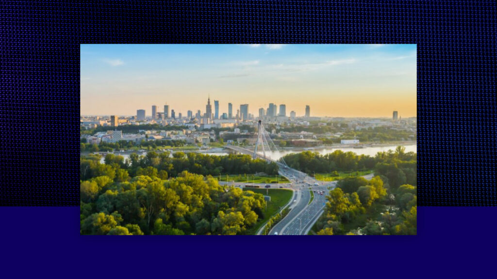 A cityscape view of Warsaw, Poland, at sunset, featuring the skyline with modern buildings, a suspension bridge over the Vistula River, and green trees in the foreground.