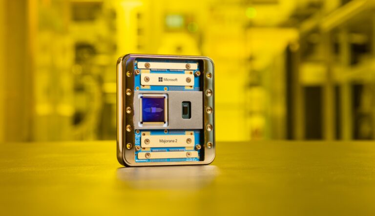 A close-up of a Microsoft quantum computer chip labeled "Majorana 2," standing upright on a surface with a yellow-tinted laboratory background out of focus.
